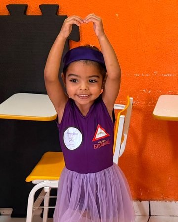 Aluna de ballet do Colégio Emanuel dentro da sala de aula, fazendo coração com as mãos