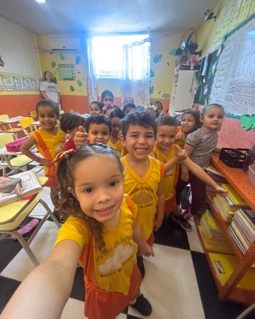 Turma da educação infantil reunida na sala de aula, de uniforme amarelo, sorrindo para a foto